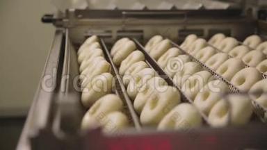 在一个小镇的甜甜圈面包店制作甜甜圈的程序-甜甜圈在油炸锅里油炸。 场景。 准备过程